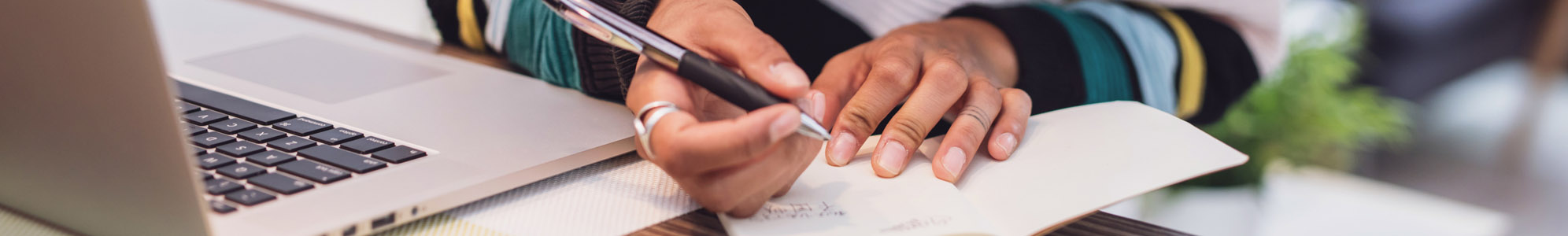 A person sitting at a desk with a laptop, taking notes on a piece of paper.