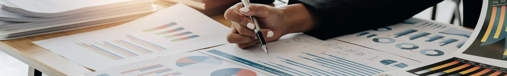 A Person with a pen looking at several graphs on paper.