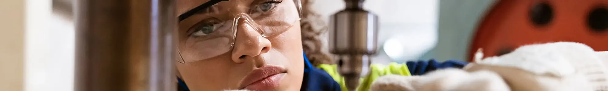 Close-up of female apprentice using yoke machine. Female engineer is wearing protective glasses in factory. She is working in manufacturing industry.