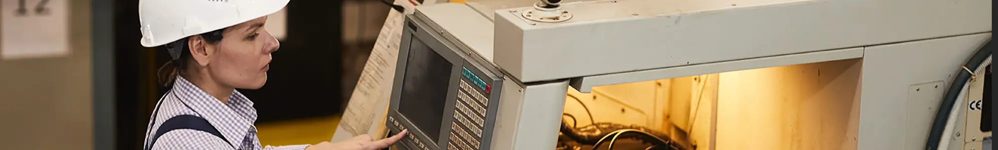 Serious busy female technical engineer standing at cnc lathe and pushing buttons while choosing CNC machining operations at factory